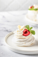 Meringues mini pavlova cake with whipped cream, fresh cherry and mint leaves on a plate, white marble background. Light summer dessert, text space
