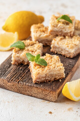 Lemon crumble bars on wooden cutting board on white textured background, oatmeal lemon bars