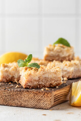 Lemon crumble bars on wooden cutting board on white tile background with copy space. Oatmeal lemon bars