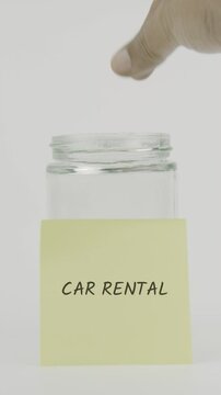 Car rental concept with a hand inserting a coin into a glass jar labeled with a yellow sticky note. Set against a clean white background in vertical screen format, symbolizing savings for vehicle rent