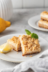 Lemon crumble bars served on a plate decorated with mint leaves on light gray background. Oatmeal lemon bars