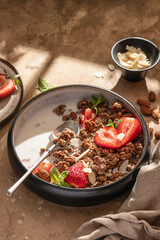 Healthy breakfast: fresh granola, muesli with milk, strawberry and almond for breakfast on brown textured background in bright morning light