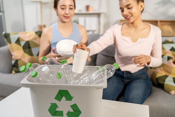 Two beautiful Asian women sorting plastic bottles for recycling at home. 