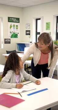 Vertical video: Teacher helping young student with homework in classroom, fostering learning