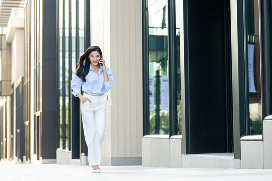 Asian young businesswoman talking on smartphone while walking in city. 