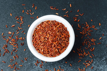 Close up of red rice in white bowl with scattered grains