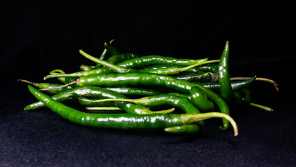 A pile of whole green chilies with dramatic studio lighting on the surface and a black background, ideal for healthy, fresh food and natural spicy seasoning themes.