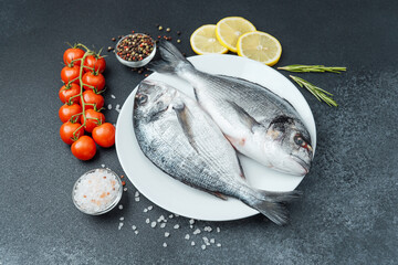 Raw dorado fish with tomatoes lemon herbs and spices on white plate