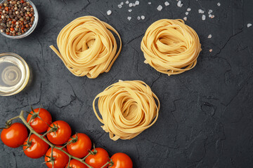 Tagliatelle pasta nests with tomatoes, oil, pepper and salt on black textured background