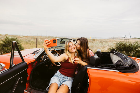 Young women taking selfie in red convertible car during summer road trip - Powered by Adobe