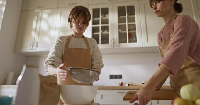 Girl sifting flour while baking with her mother in a cozy bright kitchen at home. Girl baking in the kitchen