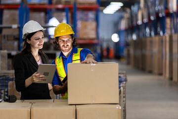 man in hard hat and safety vest assists women in scanning package while she records data during busy workday in a warehouse filled with shelves of goods.