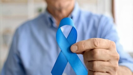 Mature man holding a light blue ribbon in hand, raising awareness for a particular illness or cause, supporting health care campaign