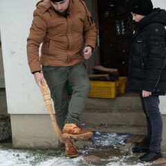 A man playfully sweeps the snow with a broom as a boy watches, creating a lighthearted winter scene...