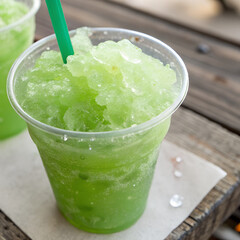 A green slush drink with a green straw on a wooden table