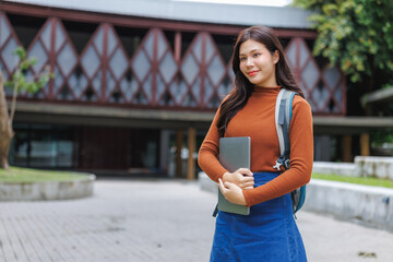 University student holding laptop and smiling on campus