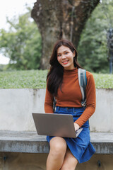 Smiling student working on laptop outdoors in university campus park