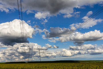 Vast landscape featuring power lines and dramatic clouds on a bright day over a yellow field in rural area
