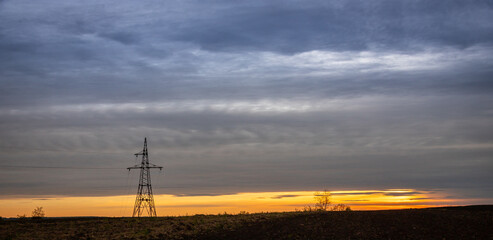 Sunset over a vast landscape with a lone power tower silhouetted against the colorful evening sky near a rural area