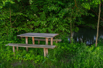 Wooden picnic table and benches set in a serene green setting beside a calm stream during late afternoon