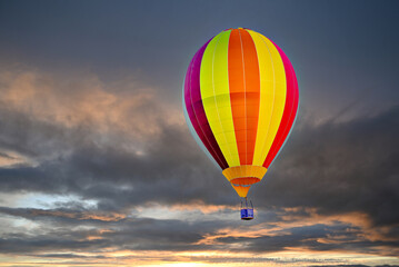 Colorful hot air balloon flying under orange sunset sky
