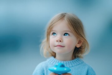 capture child curious gaze upwards as they hold small toy resembling ufo set against softly blurred background conveying