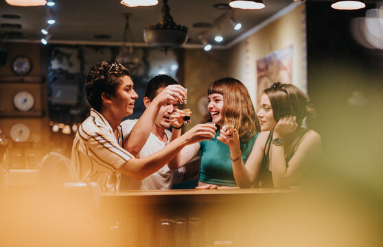 A group of young friends share laughter and happiness during a fun night out at a vibrant bar, creating joyful memories together.