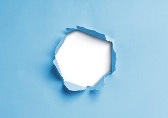Close-up image of a blue paper sheet with a jagged hole torn through the center, revealing a transparent background.