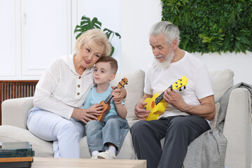 Grandparents teaching their grandson to play guitar on sofa at home