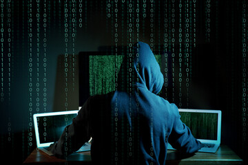 Cyber attack. Hacker working on computers in dark room. Binary code around him