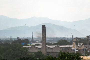 An expansive view of Madurai showcases industrial chimneys among lush greenery, with distant...