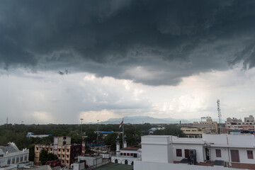Dramatic storm clouds gather over a cityscape with a distant mountain range on a quiet afternoon