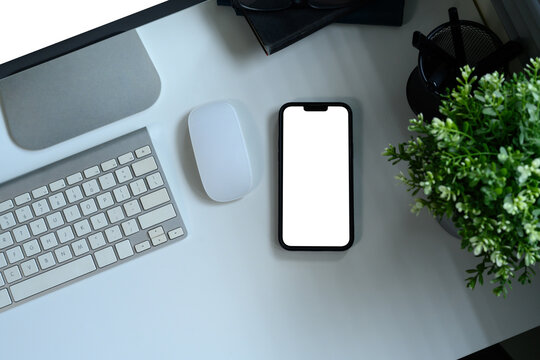 Flat lay of mobile phone, keyboard, and mouse next to green plant on desk