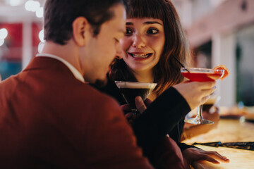 A joyful couple shares cocktails at a warm, inviting bar. They smile and enjoy each other's company, highlighting leisure and friendship in a cozy setting.