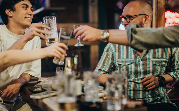 Fototapeta Close-up of friends toasting with drinks at a bar. They are laughing and enjoying a casual night out, celebrating their friendship and creating joyful memories.