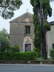 Facade Of A Weathered Old Stone Building With Cross Near Road In Sirmione, Italy