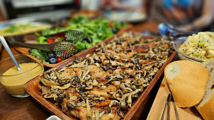 Enjoying a homemade dinner buffet — roasted chicken thigh with mushrooms and truffle oil sauce, kale salad with blueberries and cherry tomatoes, and sliced European bread on wooden table
