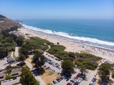 Aerial view of a crowded  Stinson Beach, California, USA. People are swimming, sunbathing, and relaxing on a sunny day. The parking lot is full of cars.
