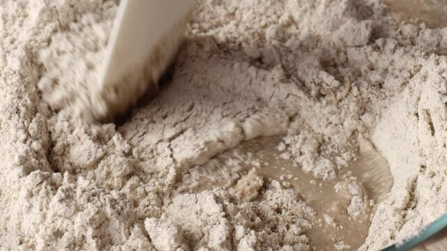 mixing flour with water using silicone spatula in glass bowl for bread dough preparation showing closeup of blending ingredients concept of bakery shop cooking blog homemade baking