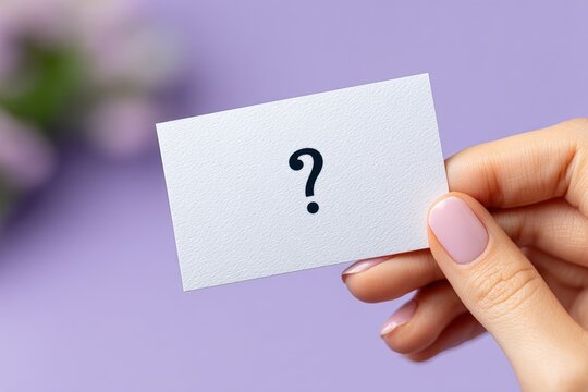 Close-up of a person's hand holding a white business card with a question mark symbol on purple background