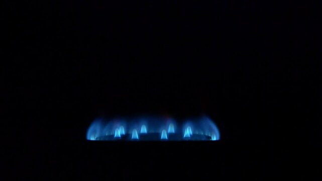 Close-up view of gas stove burner igniting and burning with blue flame in kitchen setting, no people