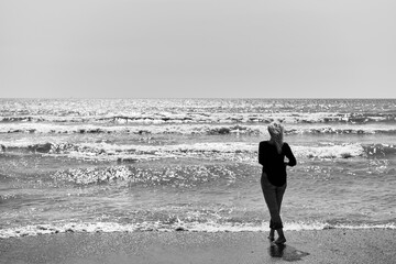 Black and white shot mature blonde woman walking on the sea enjoying the warmth and summer, light...