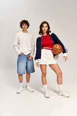 Obraz premium Stylish young couple posing confidently with a basketball in a minimalist studio setting