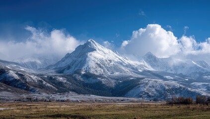 Fototapeta premium Snow-capped mountain range under a vibrant blue sky, with puffy clouds and a foreground of flat, lightly snow-dusted land