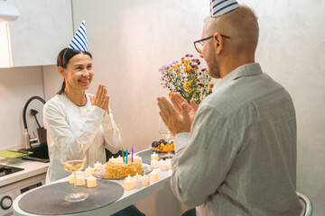 Couple Birthday Celebration Kitchen: Mature couple celebrates birthday with cake and flowers in their kitchen.