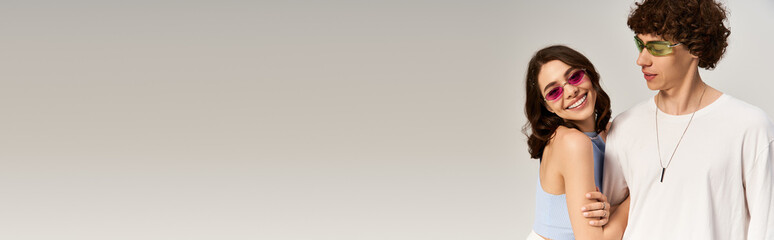 Stylish young couple shares a playful moment in bright, vibrant sunglasses and trendy outfits