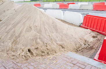 Pile of sand. Red and white plastic barriers blocking the road