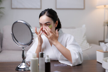 Young woman applying eye patches while looking in the mirror