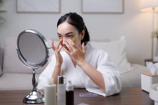 Young woman applying eye patches while looking in the mirror - Powered by Adobe