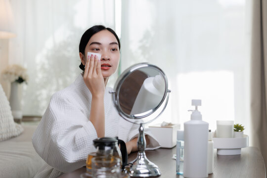Young asian woman removing makeup with cotton pad in front of mirror - Powered by Adobe